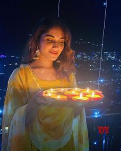 a woman holding a tray with lit candles in front of the city skyline at night