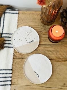 two white plates sitting on top of a wooden table next to a candle and some pine cones