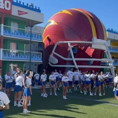 a group of people standing in front of a giant football helmet on top of a field