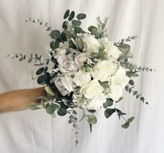 a bouquet of white flowers and greenery is held by a man's hand