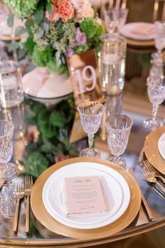 the table is set with gold and white plates, silverware, and floral centerpieces