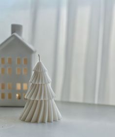 a small white christmas tree sitting next to a miniature house on a window sill