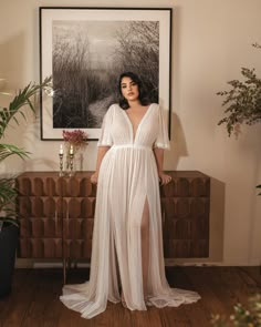 a woman standing in front of a painting wearing a white dress with high slits