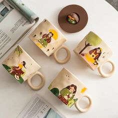 four coffee mugs sitting on top of a table next to a pen and paper