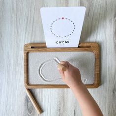 a child's hand is drawing on the sand in front of a wooden frame