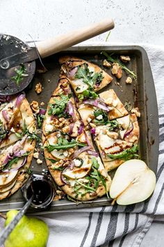 an apple and goat cheese pizza on a baking sheet with a knife, fork and napkin