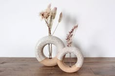 two white vases sitting on top of a wooden table next to each other with dried flowers in them