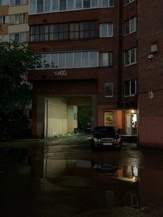 a car is parked in front of a building on a rainy night with its lights on