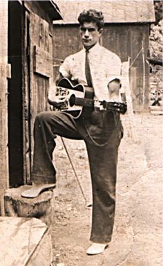 an old black and white photo of a young man holding a guitar in his right hand