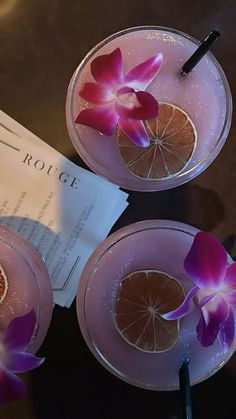 two glasses filled with drinks and garnished with flowers on the rims, sitting on a table