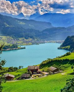 a lake in the middle of a green valley with mountains in the background and clouds in the sky