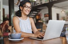 a woman sitting at a table with a laptop computer in front of her, smiling