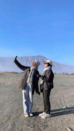 two people standing in the sand with their arms up