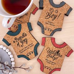 three baby onesuits on cork coasters next to a cup of tea