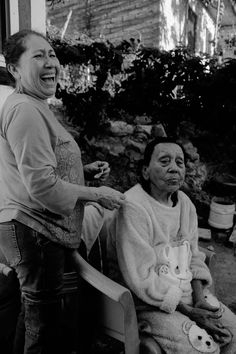 an old woman sitting in a chair next to another woman who is holding a teddy bear