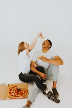 a man and woman sitting on the floor eating pizza