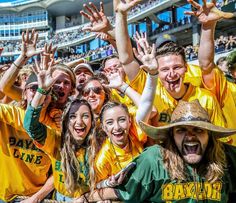 a group of people in yellow shirts and hats at a sporting event with their hands up