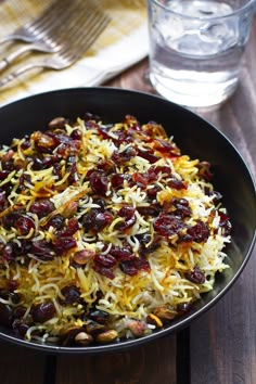 a black bowl filled with lots of food next to a glass of water on top of a wooden table