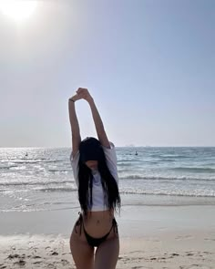 a woman standing on top of a sandy beach next to the ocean with her arms in the air