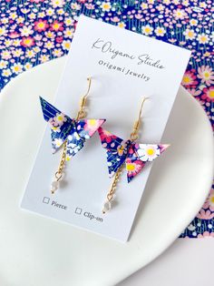 the origami butterfly earrings are sitting on top of a white plate with flowers