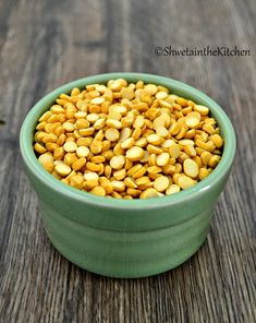 a green bowl filled with corn kernels on top of a wooden table next to a plant