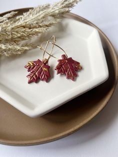 - Maple Leaf Hoops- Embrace the beauty of autumn all year round with our exquisite Handmade Crimson Red Maple Leaf Earrings. Crafted from high-quality polymer clay and adorned with delicate hints of gold leaf, these earrings are a stunning tribute to nature's vibrant palette. Product Details: Materials: Each earring is meticulously handmade using lightweight polymer clay, ensuring comfort and durability. The striking crimson red is complemented by shimmering gold leaf accents, adding a touch of elegance and sophistication. Design: The intricate maple leaf design captures the essence of fall, with detailed veins and contours that mimic the beauty of real leaves. The gold accents catch the light beautifully, creating a stunning visual effect that will turn heads. Care Instructions: Wipe gent Clay Leaf Earrings, Fall Clay Earrings, Earrings Handmade Clay, Clay Leaf, Maple Leaf Design, Handmade Clay Earrings, Earrings Fall, Earrings Clay, Red Maple