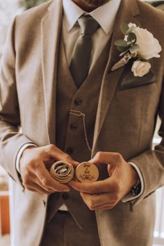 a man wearing a suit and tie holding a small badge in his hand while standing next to a window