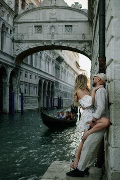 a man and woman leaning against a wall next to a canal with gondola in the background