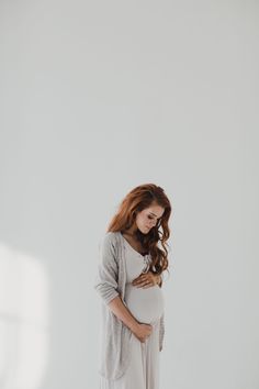 a pregnant woman standing in front of a white wall with her hands on her stomach