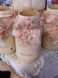 three mason jars with pink flowers and lace on them sitting on a doily covered table