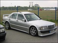 a silver mercedes benz is parked in front of a fence