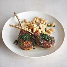 a white plate topped with meat covered in pesto and pine nuts next to beans