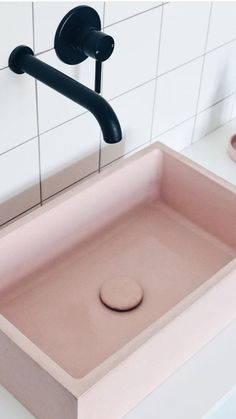 a pink sink in a bathroom with black faucet and white tiled wall behind it