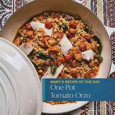 a pan filled with pasta and tomatoes on top of a table cloth next to a white pot