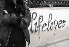 a woman with her arms crossed standing in front of a wall that has graffiti on it