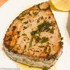 a piece of meat on a white plate with lemon wedges and parsley next to it