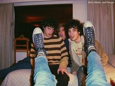 two young men sitting on top of a bed with their feet up in the air