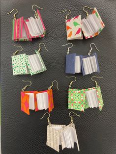 six book earrings are displayed on a black surface, each with different patterns and colors