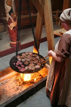 a woman standing next to a grill with food cooking on it in front of her