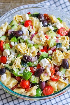 a glass bowl filled with pasta salad on top of a checkered table cloth next to a fork