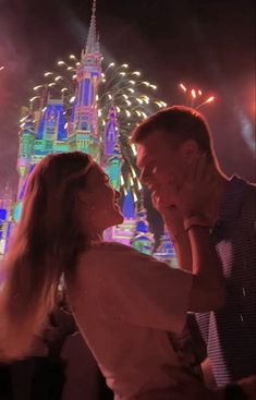 a man and woman standing next to each other in front of a castle at night