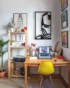 a laptop computer sitting on top of a wooden desk next to a yellow chair and potted plant