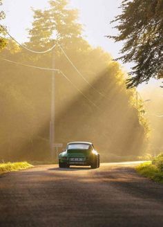 a car driving down a country road with the sun shining on it's side