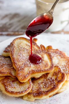 pancakes with powdered sugar and syrup being drizzled over them on a white plate