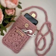 a crocheted cell phone case sitting on top of a table next to flowers