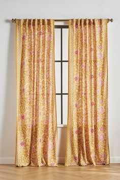 an open window with yellow curtains and pink flowers on the drapes, in front of a white wall