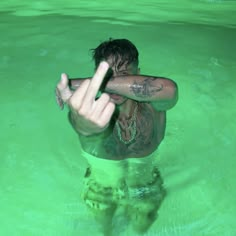 a man in the water with his arm raised up and tattoos on his chest pointing at something