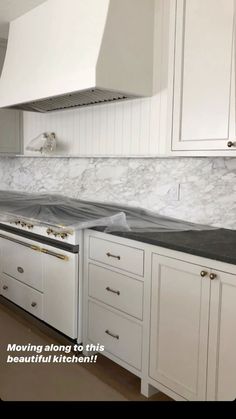 a kitchen with white cabinets and marble counter tops, along with an oven hood over the range