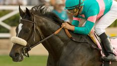 a man riding on the back of a brown horse down a race track with spectators in the background