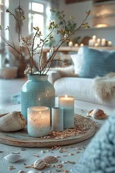 some candles are sitting on a table with shells and flowers in a blue glass vase